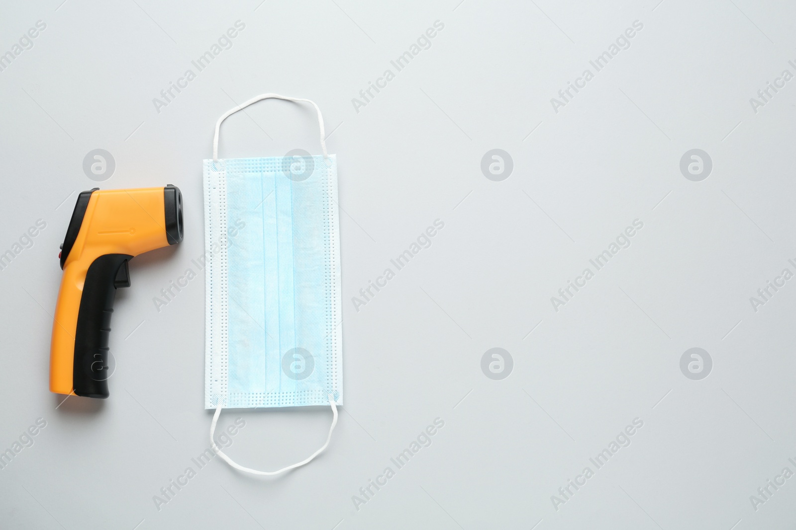 Photo of Infrared thermometer and medical mask on grey background, flat lay with space for text. Checking temperature during Covid-19 pandemic