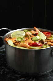 Saucepan with delicious Tom Yum soup on black marble table, closeup