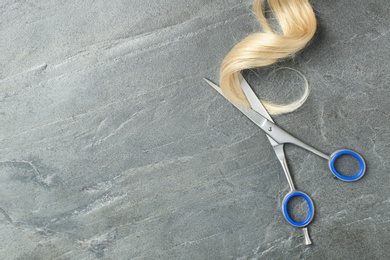 Photo of Flat lay composition with strand of blond hair, scissors and space for text on grey background. Hairdresser service