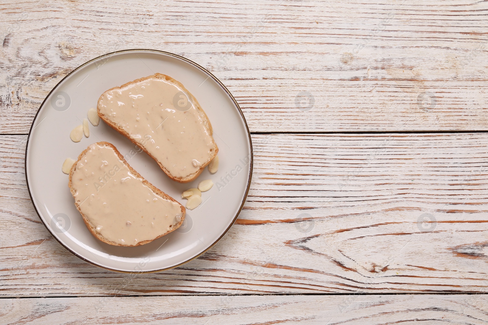 Photo of Toasts with tasty nut butter and almond flakes on light wooden table, top view. Space for text