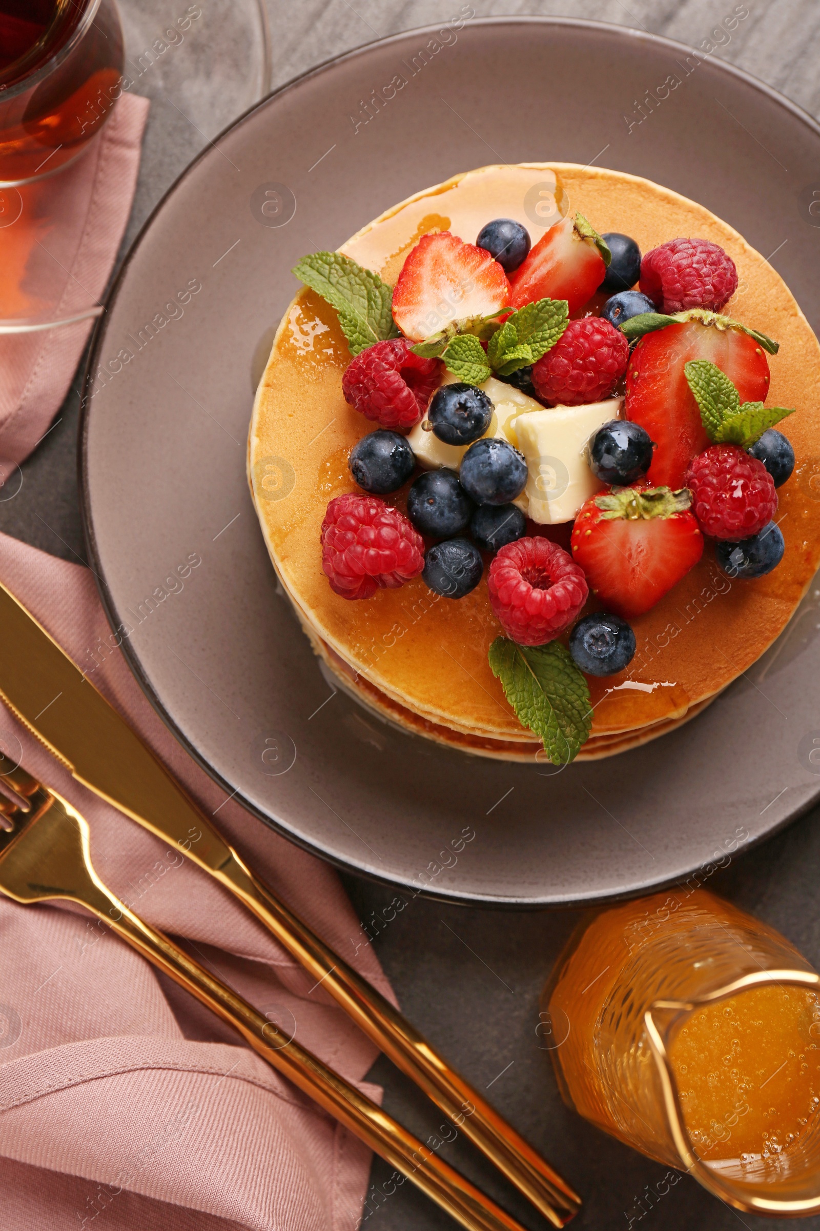 Delicious pancakes with fresh berries, honey and butter served on grey table, flat lay Photo of Delicious pancakes with fresh berries, honey and butter served on grey table, flat lay