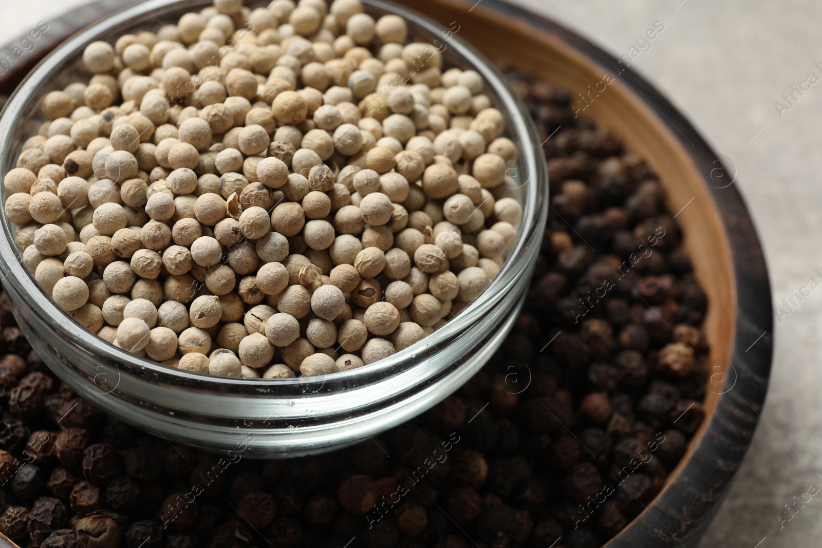 Photo of Aromatic spice. White and black peppers in bowls on light grey table, closeup