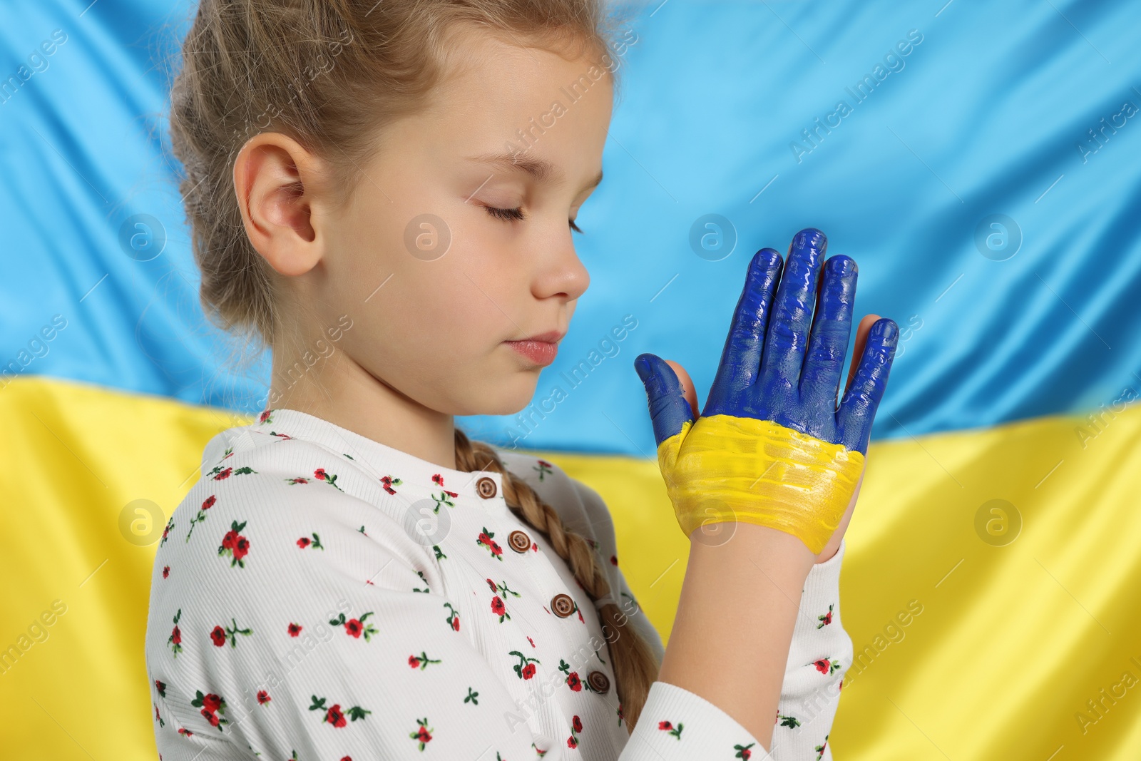 Photo of Little girl with clasped painted hands near Ukrainian flag