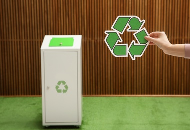 Closeup view of woman with recycling symbol and blurred trash bin on background. Space for text