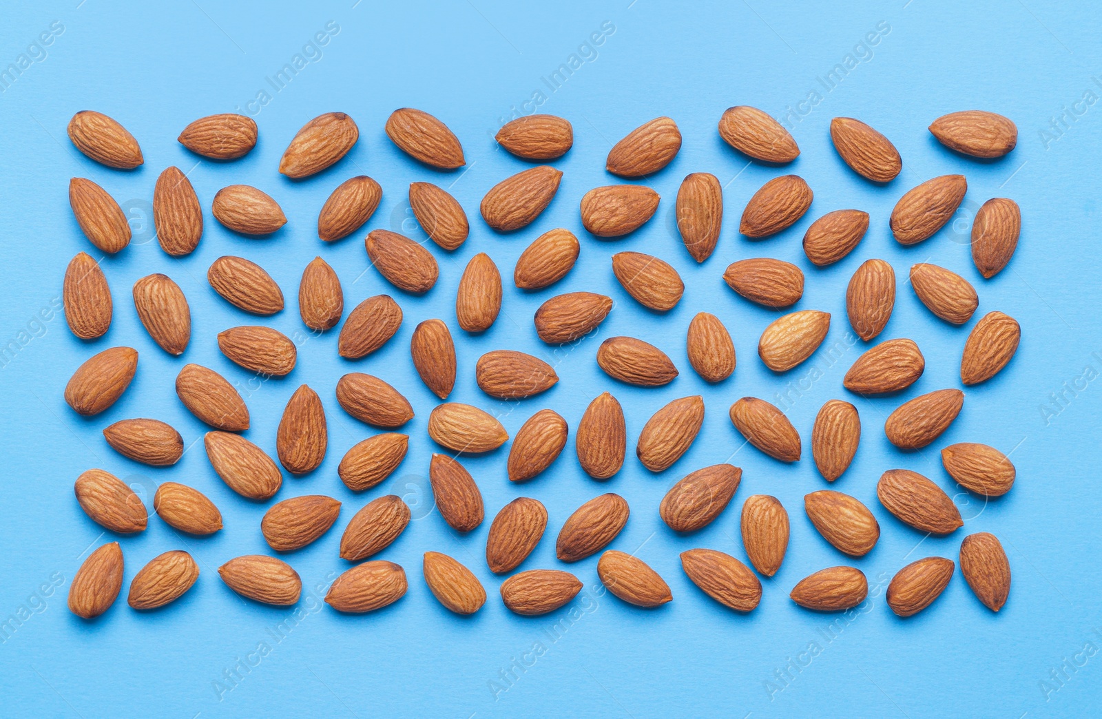 Photo of Delicious raw almonds on light blue background, flat lay