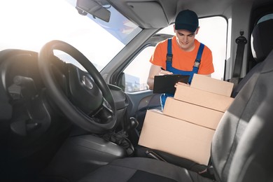 Courier with clipboard checking packages in car