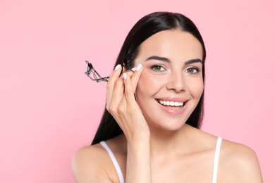 Photo of Beautiful young woman with eyelash curler on light pink background