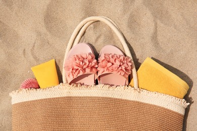 Stylish bag with beach accessories on sand, top view