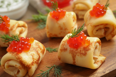 Delicious thin pancakes with red caviar on wooden board, closeup