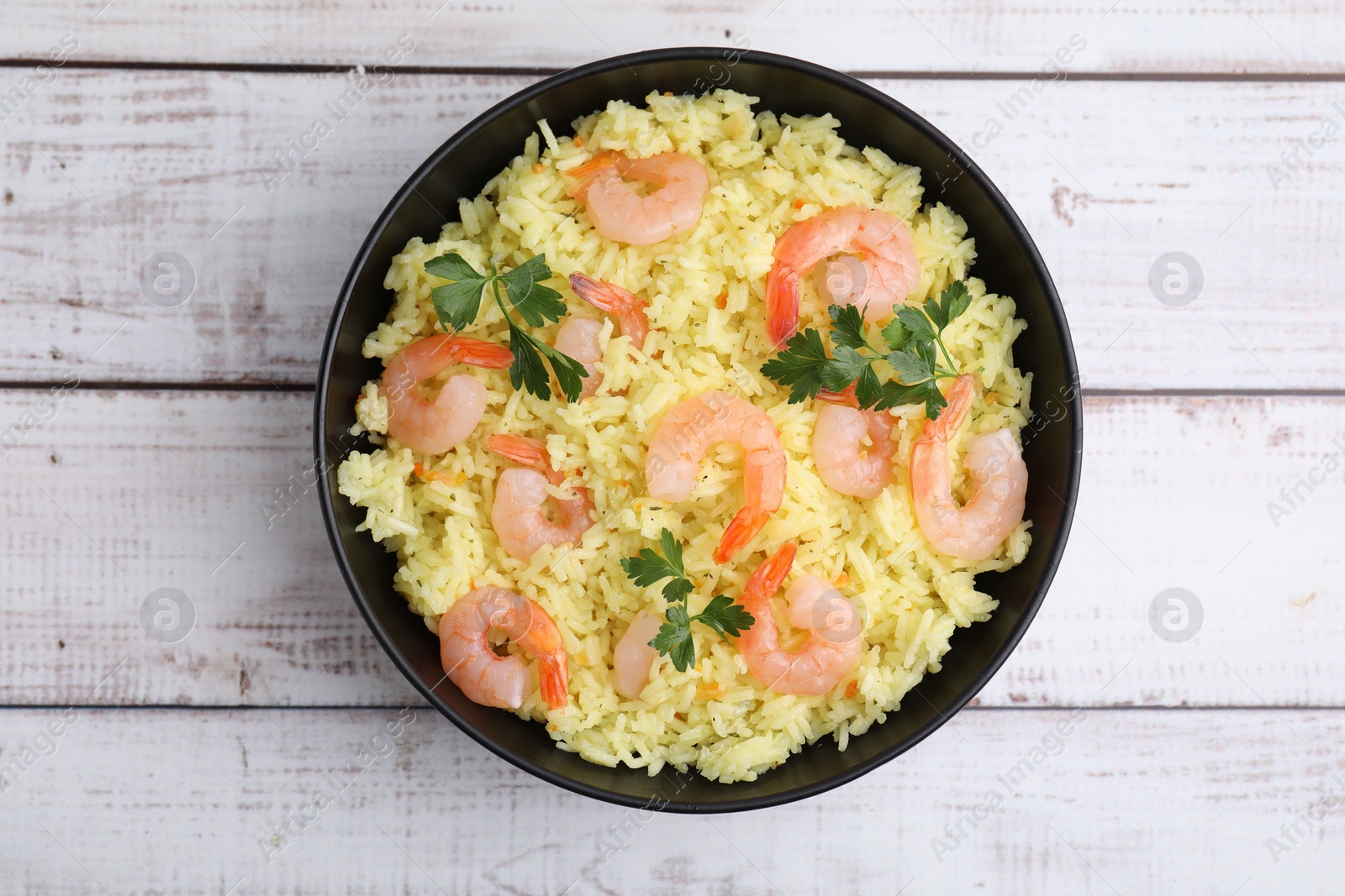 Photo of Delicious risotto with shrimps and parsley in bowl on white wooden table, top view