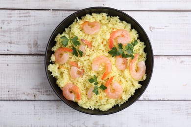 Photo of Delicious risotto with shrimps and parsley in bowl on white wooden table, top view