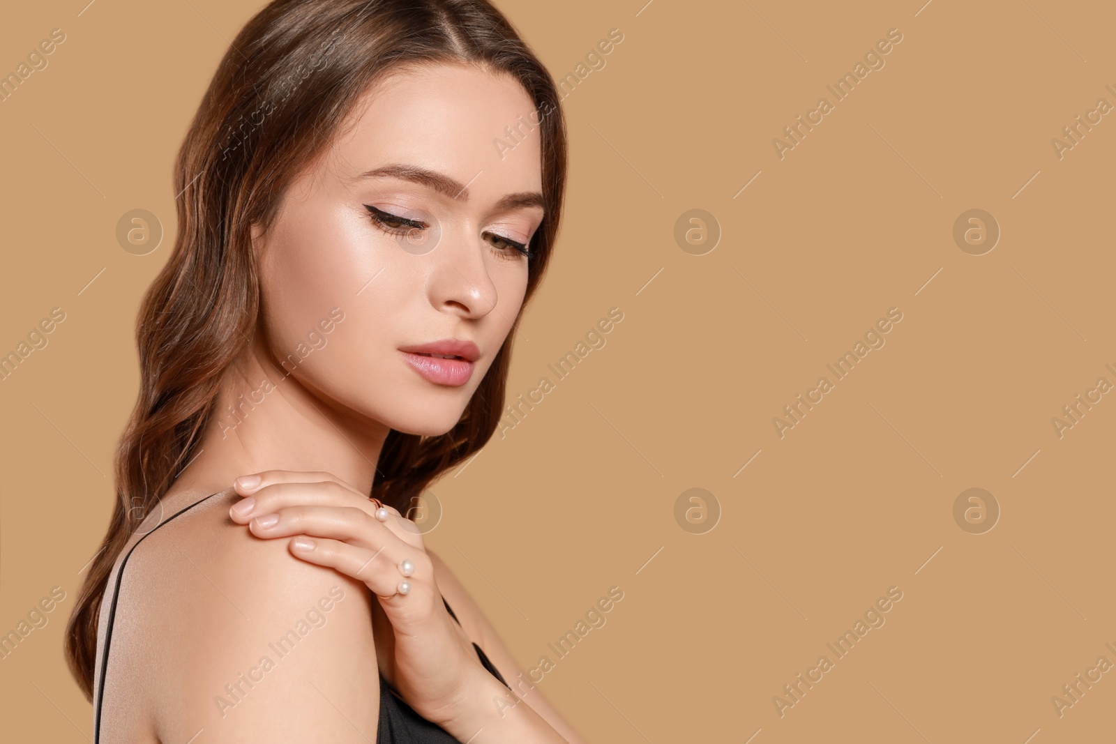 Photo of Young woman with elegant rings with pearls on brown background, space for text