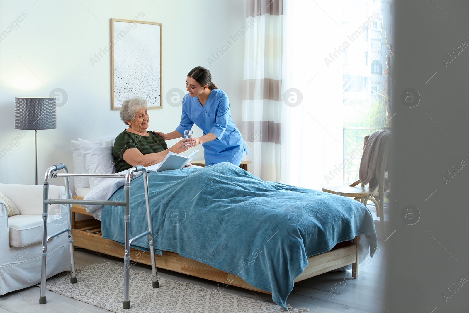 Photo of Care worker giving water to elderly woman in geriatric hospice