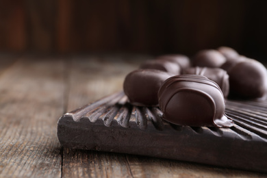 Tasty dark chocolate candies on wooden board, closeup