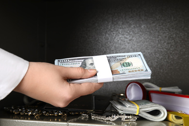 Photo of Woman putting money into steel safe, closeup