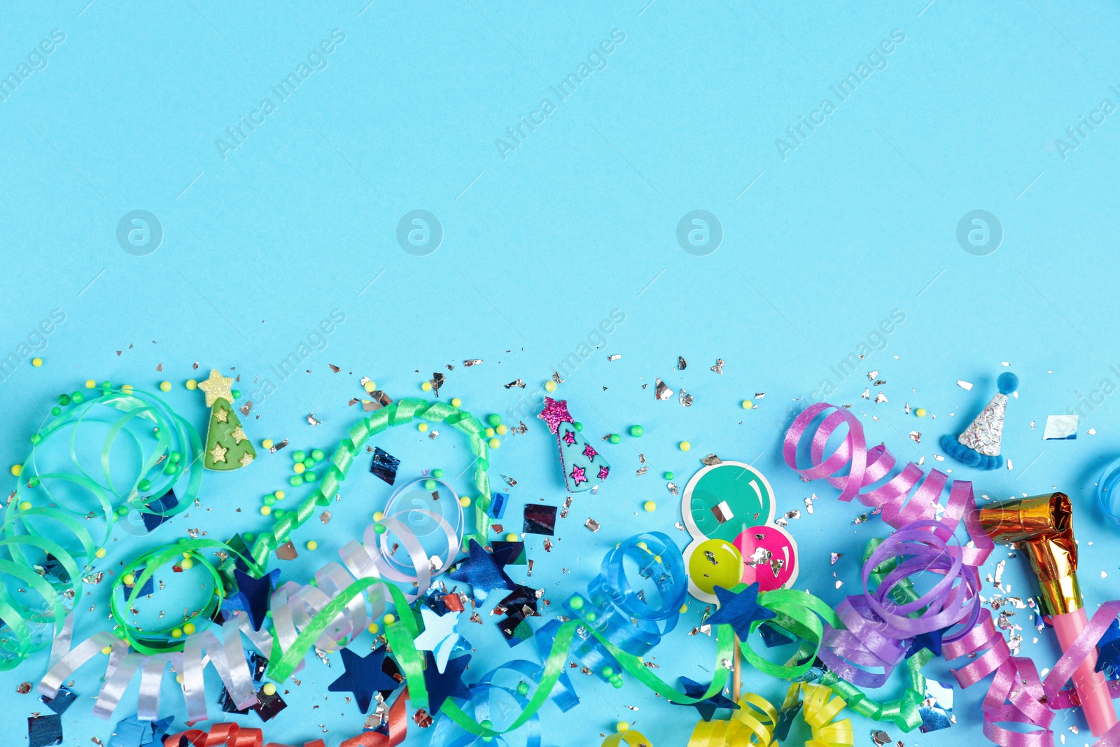 Photo of Colorful serpentine streamers, confetti and party horn on light blue background, flat lay. Space for text