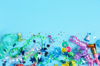 Photo of Colorful serpentine streamers, confetti and party horn on light blue background, flat lay. Space for text