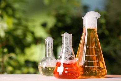 Photo of Laboratory glassware with colorful liquids on white table outdoors, space for text. Chemical reaction