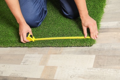 Man measuring artificial grass carpet indoors, closeup. Space for text