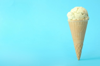 Photo of Delicious ice cream in waffle cone on light blue background. Space for text