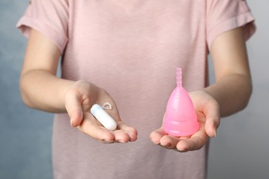 Photo of Woman holding menstrual cup and tampon on light blue background, closeup