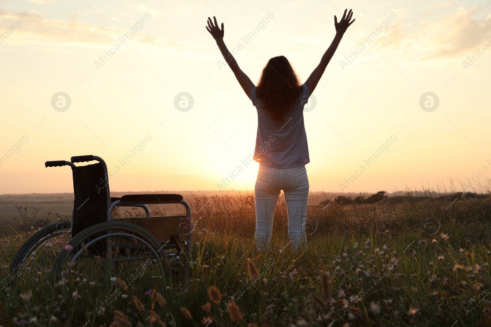 Photo of Woman standing near wheelchair in evening outdoors, back view. Healing miracle