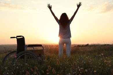 Woman standing near wheelchair in evening outdoors, back view. Healing miracle