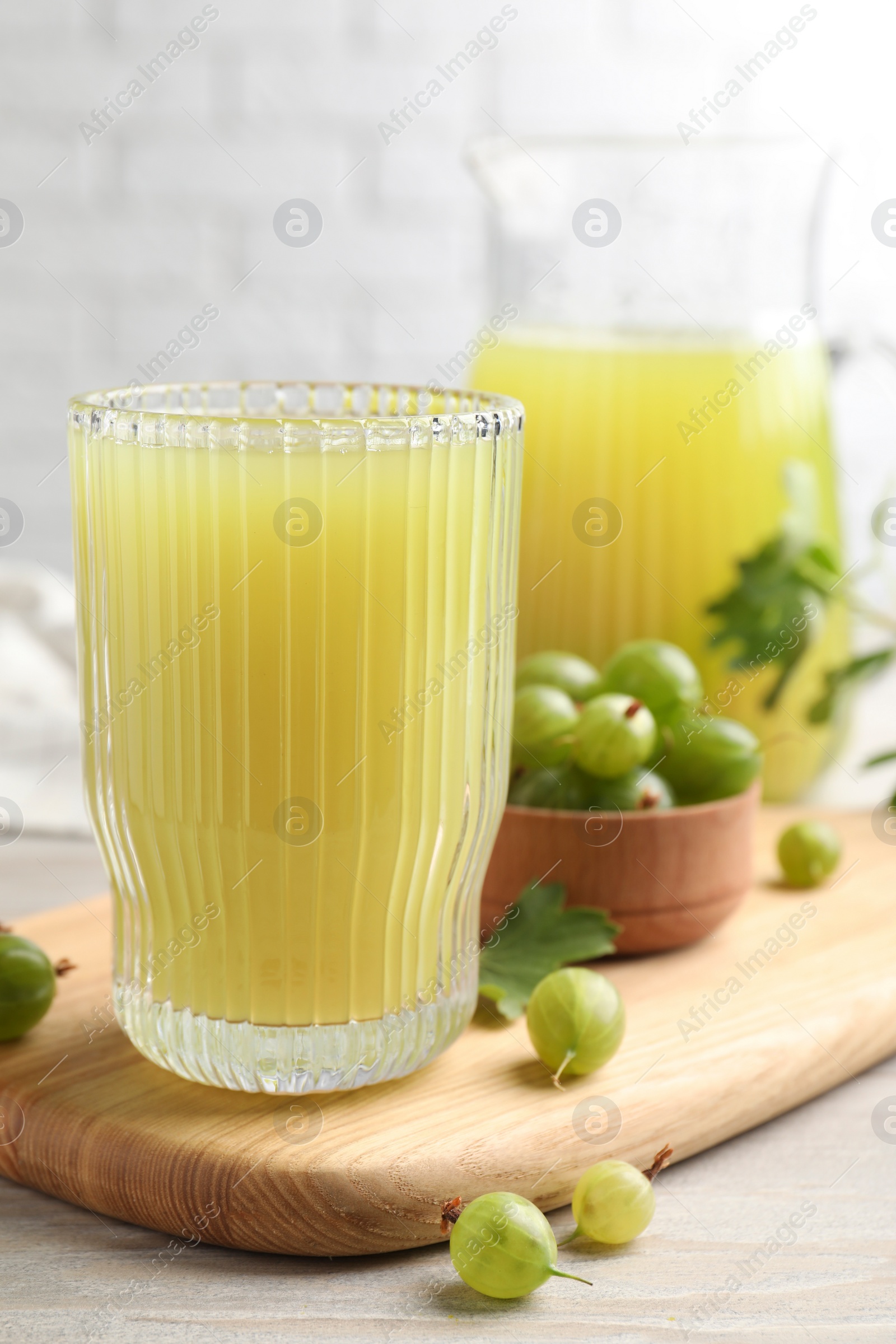 Photo of Tasty gooseberry juice and fresh berries on light wooden table, closeup