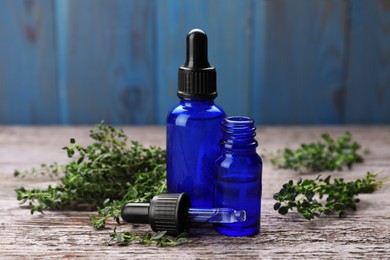 Photo of Bottles of thyme essential oil and fresh plant on wooden table