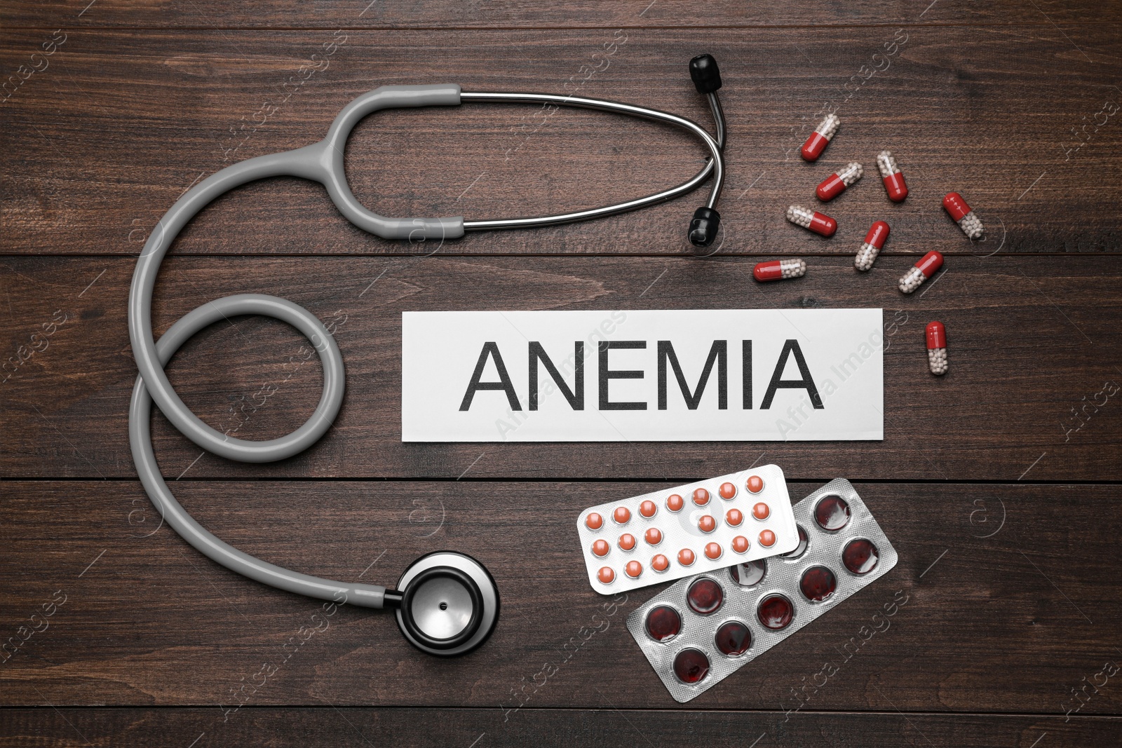 Photo of Card with word Anemia, stethoscope and pills on wooden table, flat lay
