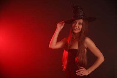 Photo of Young woman wearing witch costume on dark background, space for text. Halloween party