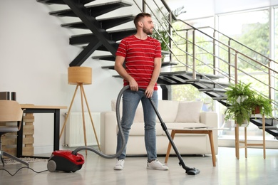 Photo of Young man using vacuum cleaner in living room