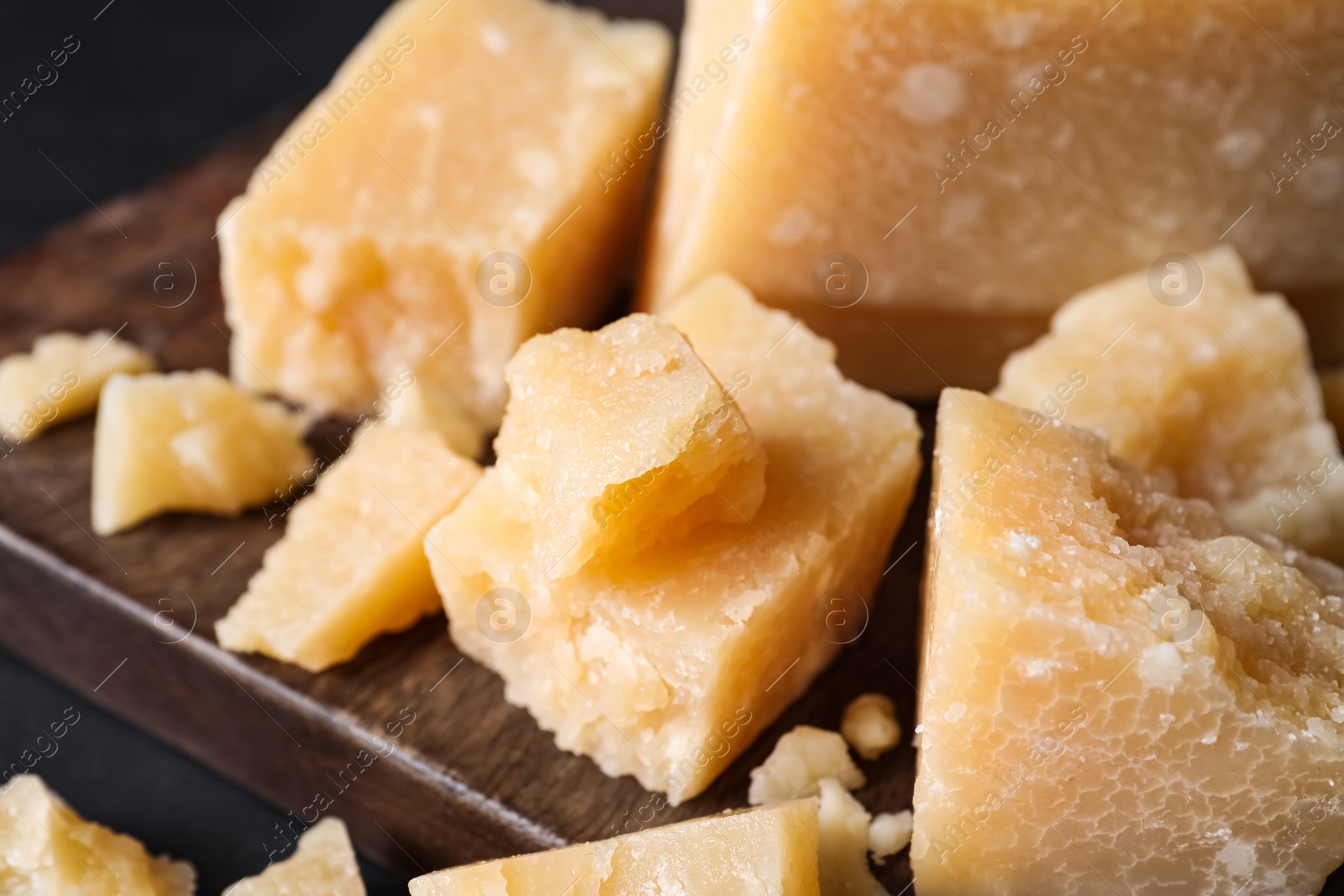 Photo of Pieces of delicious parmesan cheese on wooden board, closeup