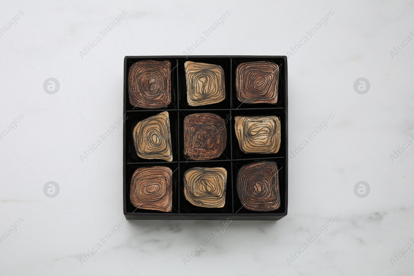 Photo of Box of tasty chocolate candies on white marble table, top view