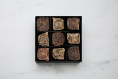 Photo of Box of tasty chocolate candies on white marble table, top view