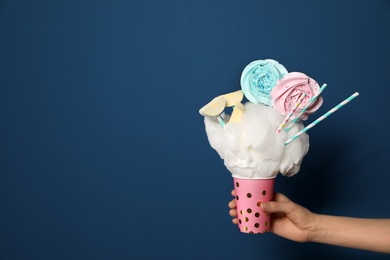 Woman holding tasty cotton candy dessert on blue background, closeup. Space for text