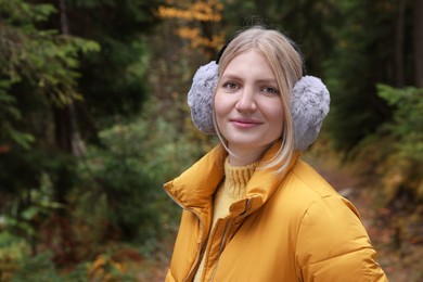 Photo of Young beautiful woman wearing warm earmuffs in forest