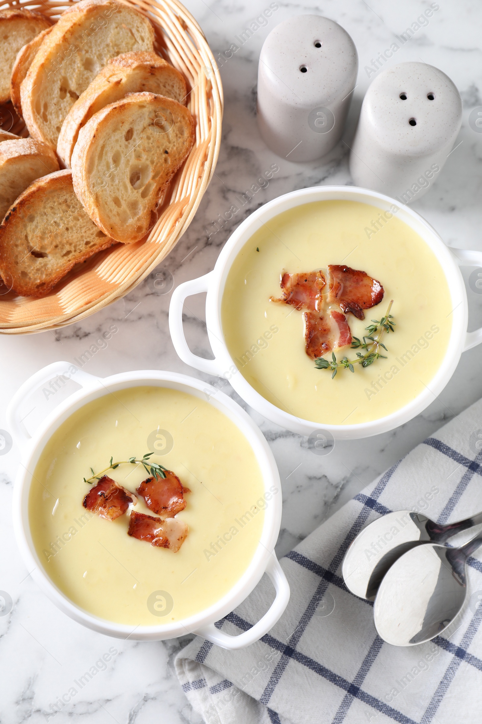 Photo of Tasty potato soup with bacon and rosemary in bowls served on white marble table, flat lay