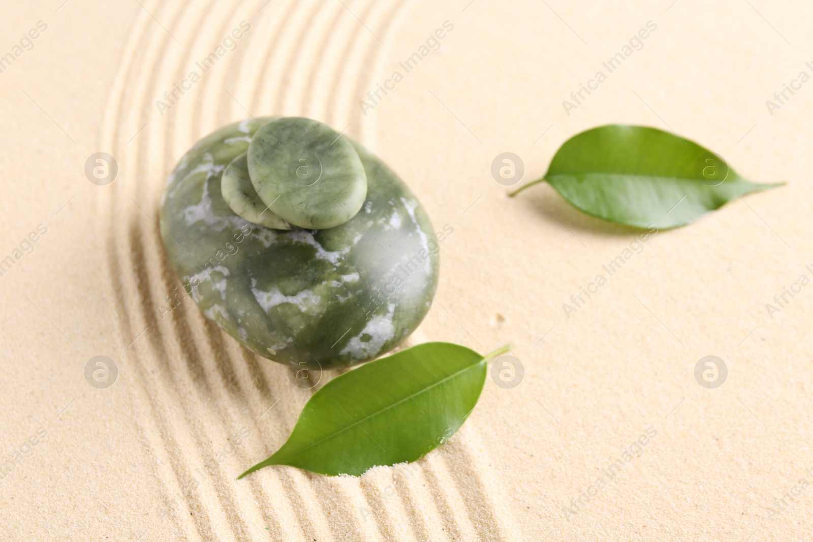 Photo of Zen garden stones and leaves on beige sand with pattern