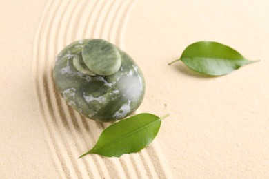 Photo of Zen garden stones and leaves on beige sand with pattern