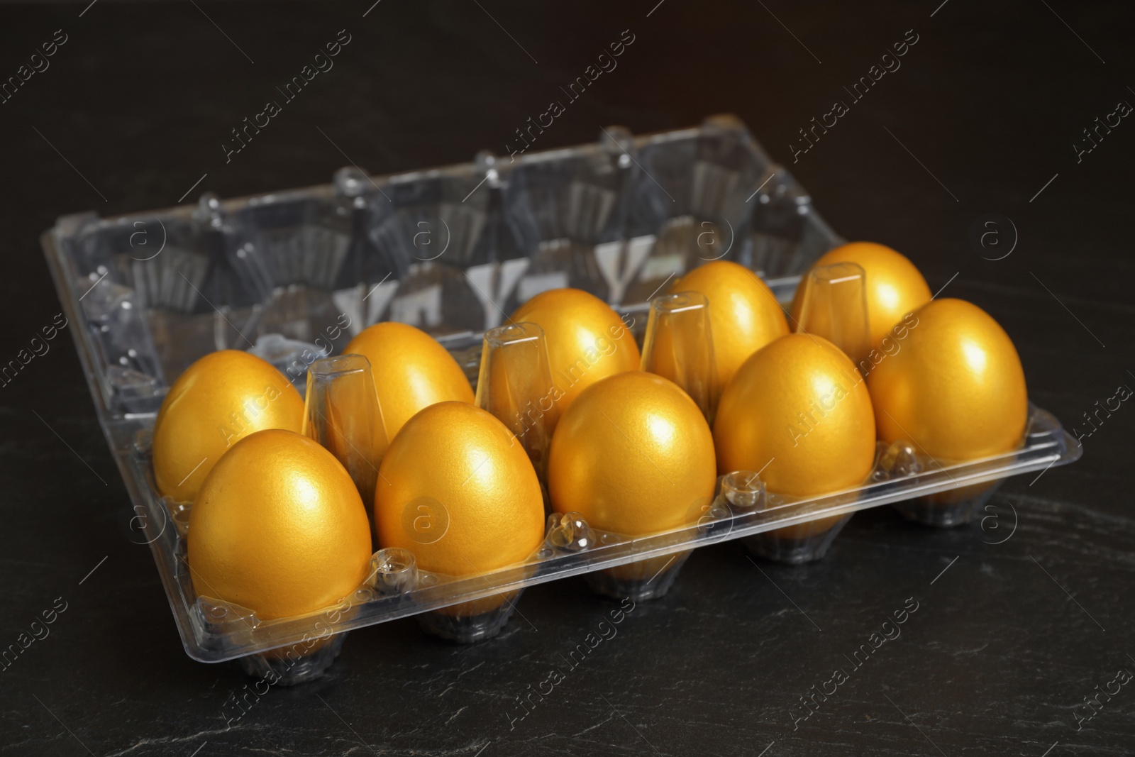 Photo of Shiny golden eggs in plastic box on black table