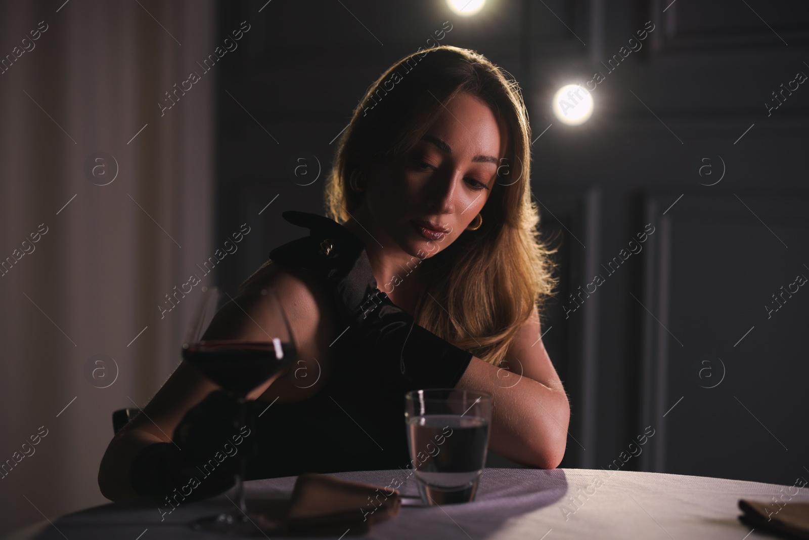 Photo of Elegant young woman with glass of wine at table indoors in evening