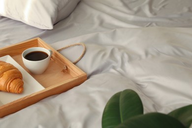 Photo of Tasty croissant and aromatic coffee on bed with stylish silky linens, space for text