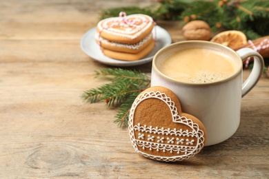 Photo of Tasty heart shaped gingerbread cookie and hot drink on wooden table. Space for text
