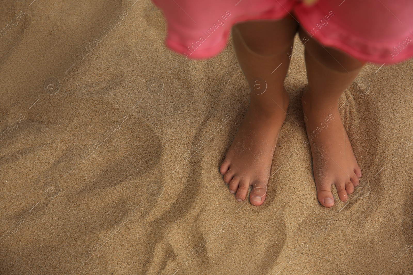 Photo of Little girl standing on sandy beach, closeup. Space for text