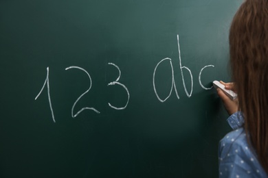 Little child writing letters and numbers on chalkboard, closeup