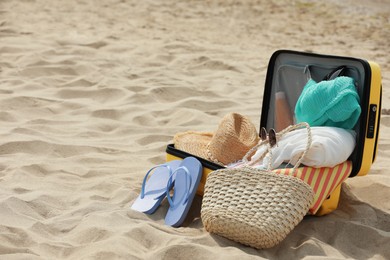 Open suitcase with beach items on sand, space for text