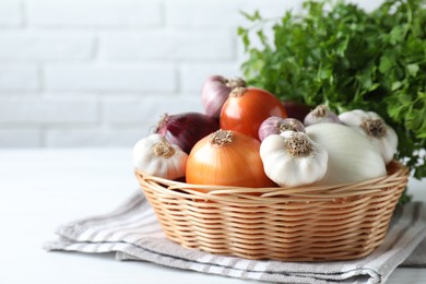 Photo of Fresh raw garlic and onions in wicker basket on white table, closeup. Space for text