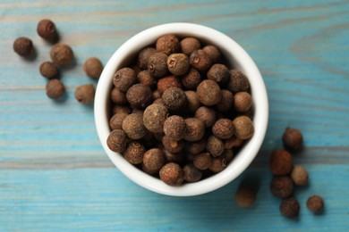Photo of Aromatic allspice pepper grains in bowl on light blue wooden table, top view