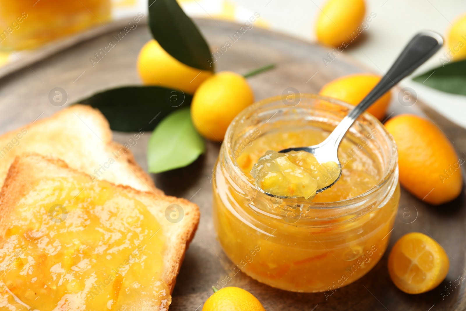 Photo of Delicious kumquat jam in jar, tasty toasts and fresh fruits on wooden board